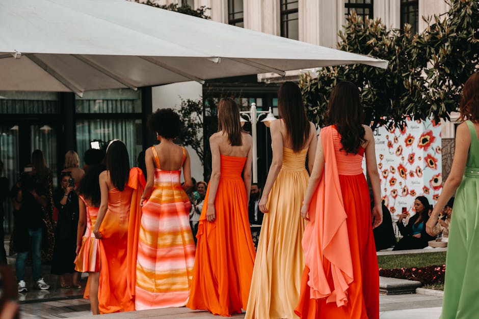 Models in stunning vibrant dresses walk the runway in an outdoor fashion show.
